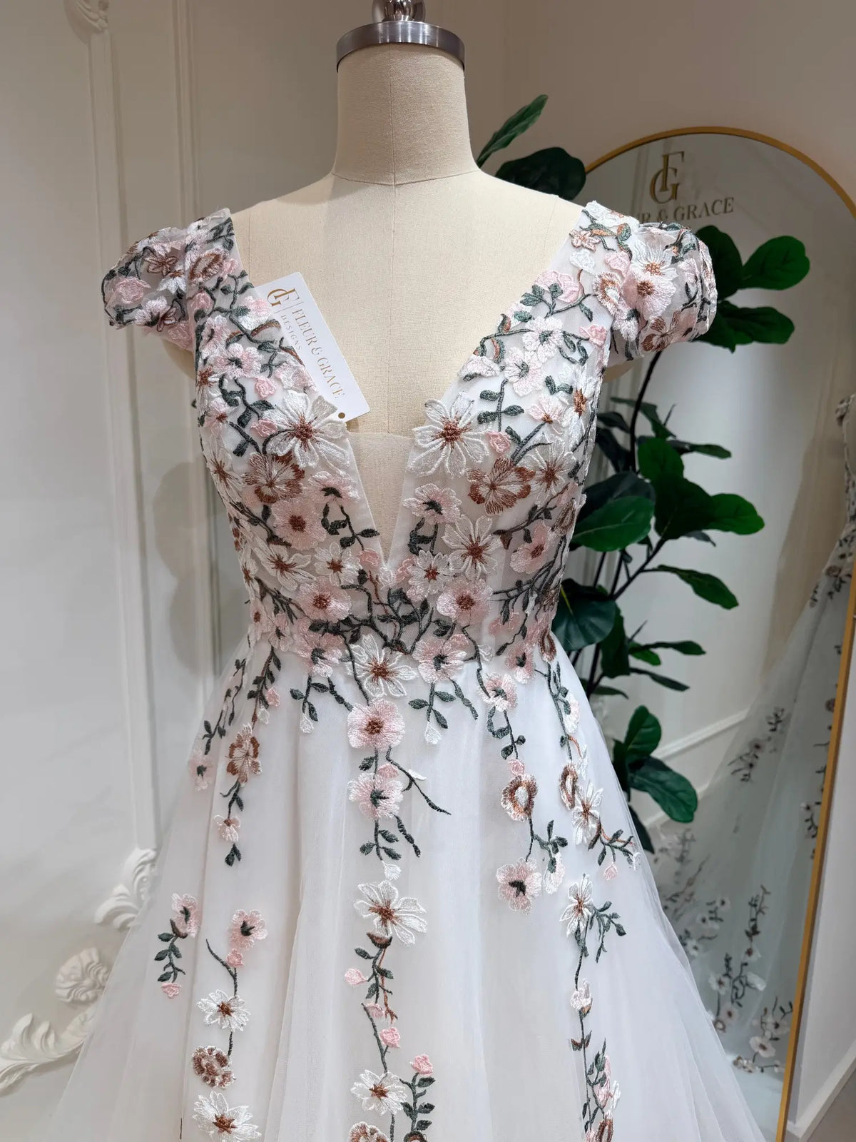 A-line wedding gown with cap sleeves, illusion V-neck, and pink 3D floral embroidery on white tulle.