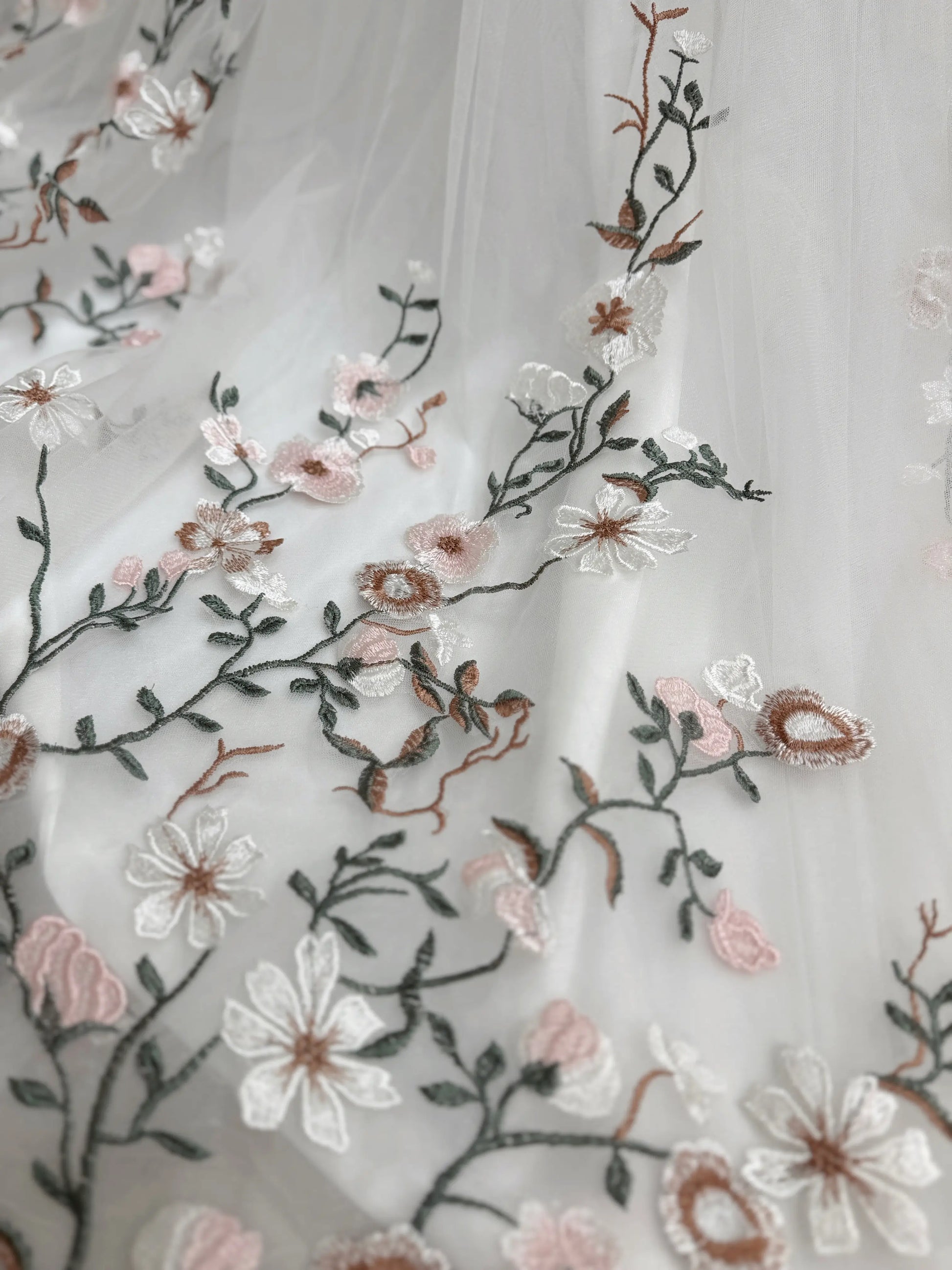 Bride mannequin wearing the Kate Gown by Fleur&Grace Designs – white tulle wedding dress with meadow floral embroidery, V‑neckline, lace‑up back, pockets, and chapel‑length train.