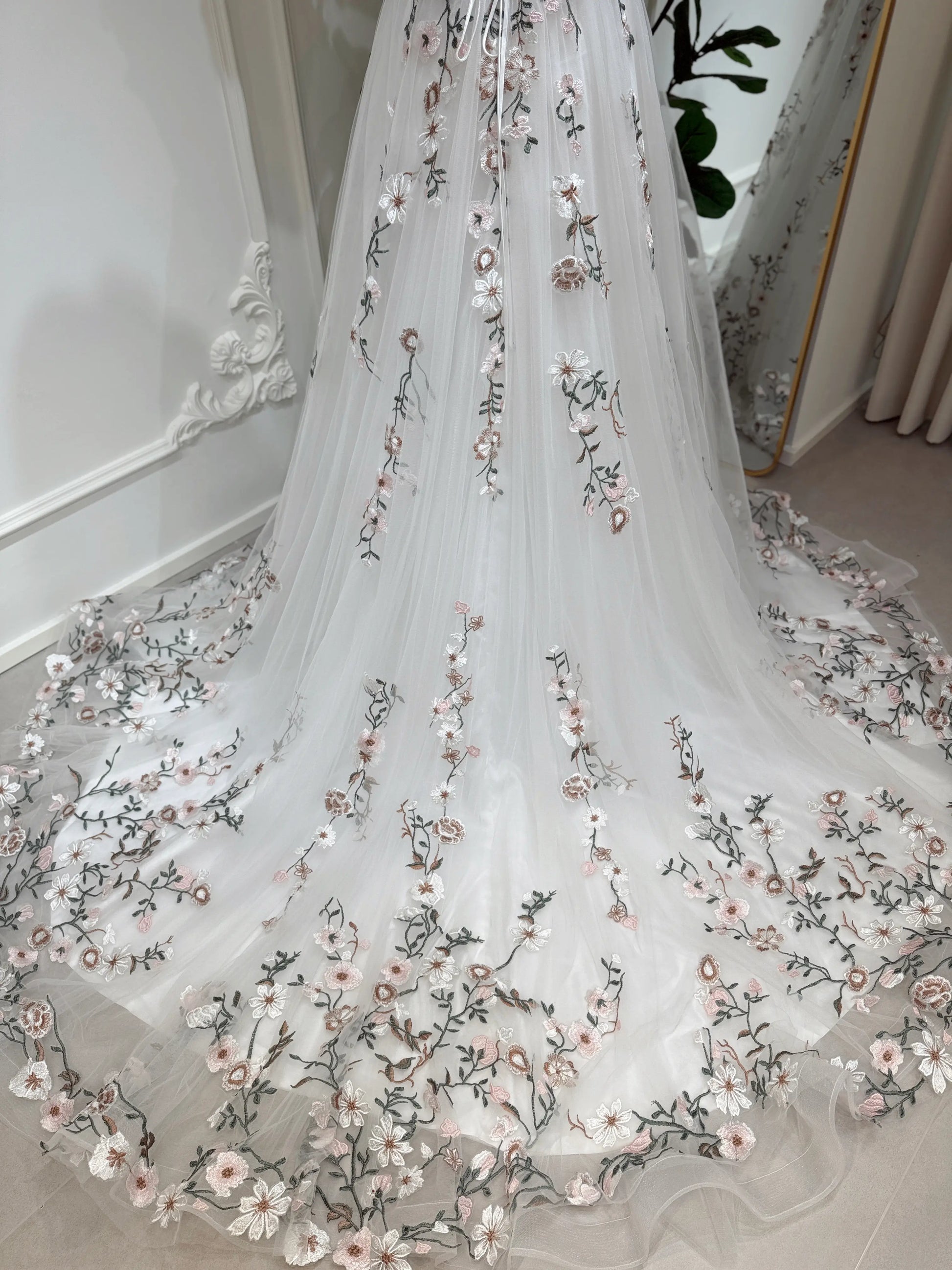 Bride mannequin wearing the Kate Gown by Fleur&Grace Designs – white tulle wedding dress with meadow floral embroidery, V‑neckline, lace‑up back, pockets, and chapel‑length train.