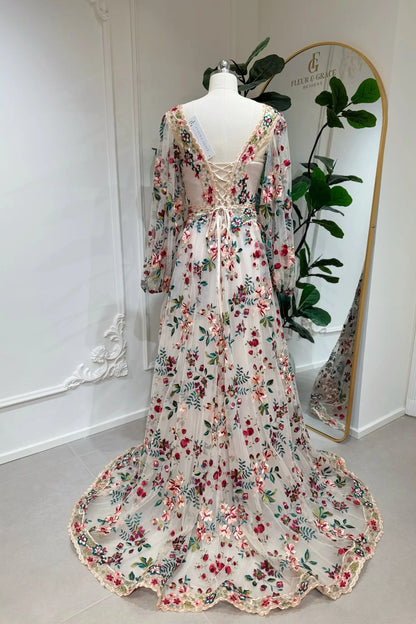 Ferry Gown by Fleur&Grace Designs — whimsical colorful floral wedding dress with pink and burgundy embroidery, long puff sleeves, lace-up back, invisible pockets, and sweep train for forest or elopement weddings.