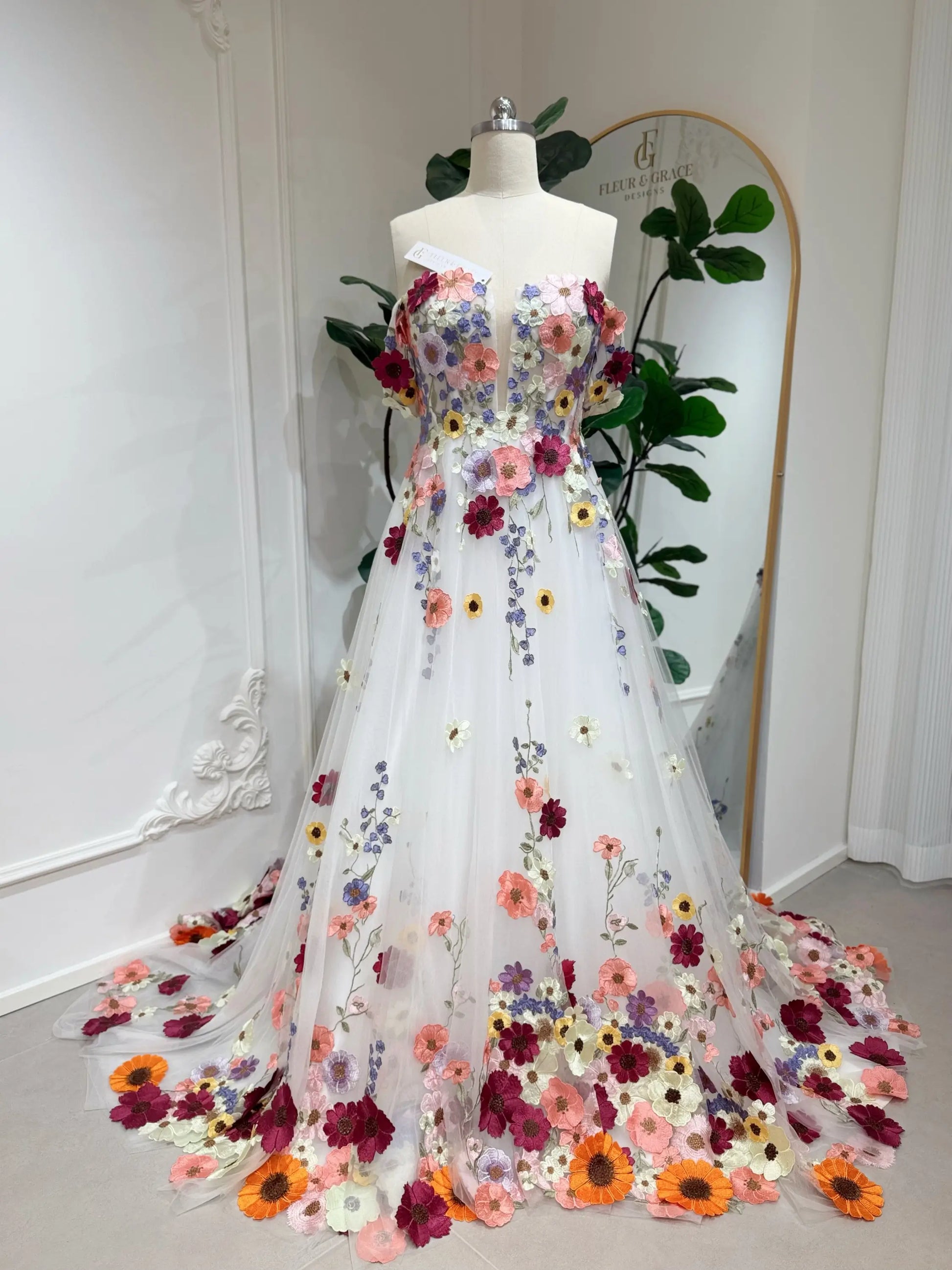 Amber Gown by Fleur&Grace Designs — off-white tulle wedding dress with colorful floral embroidery, off-the-shoulder neckline, plunging V-neck, hidden pockets, and chapel-length train for whimsical and garden weddings.