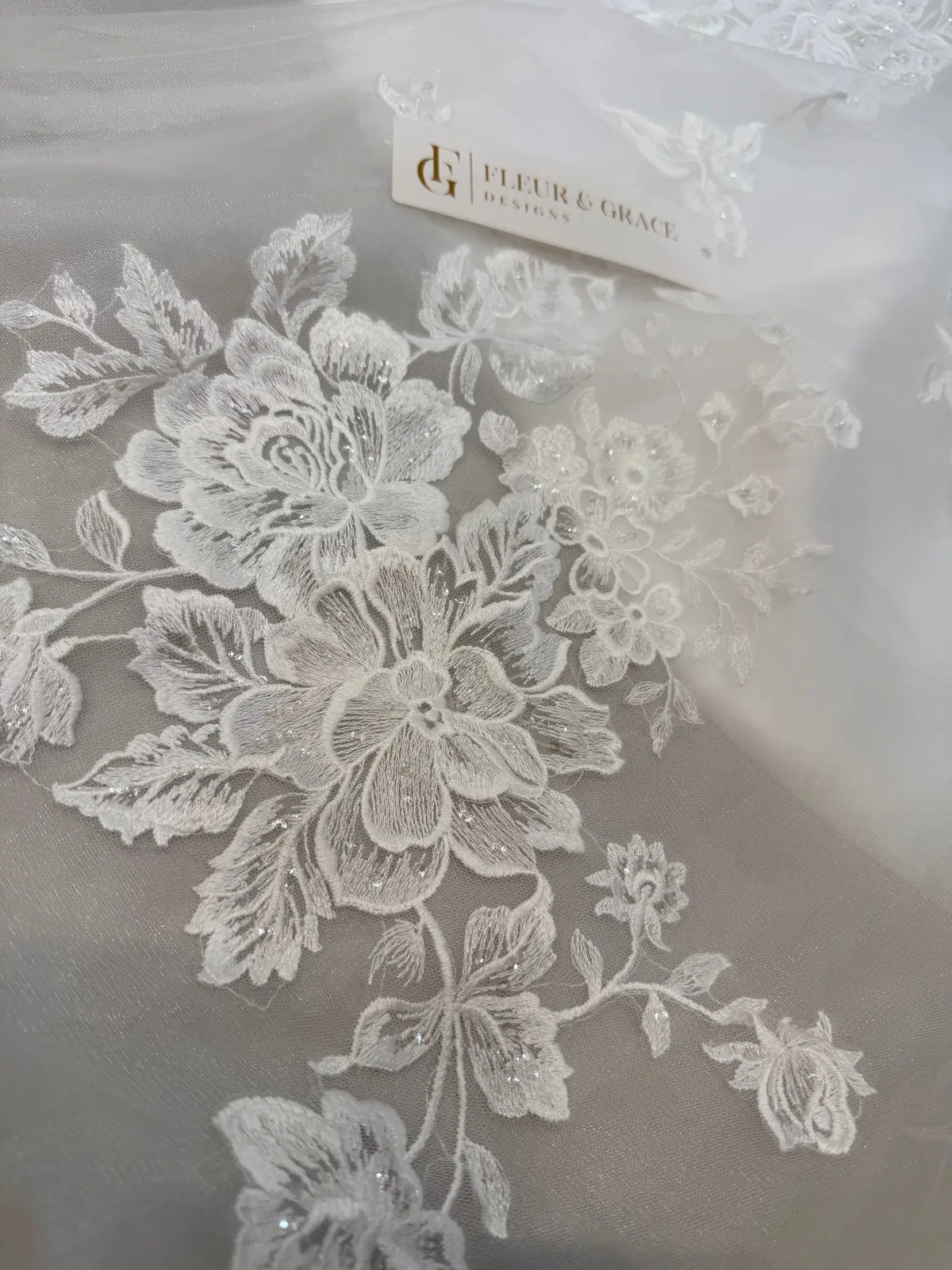 White floral lace appliqué with delicate beadwork on sheer tulle fabric for a wedding dress.
