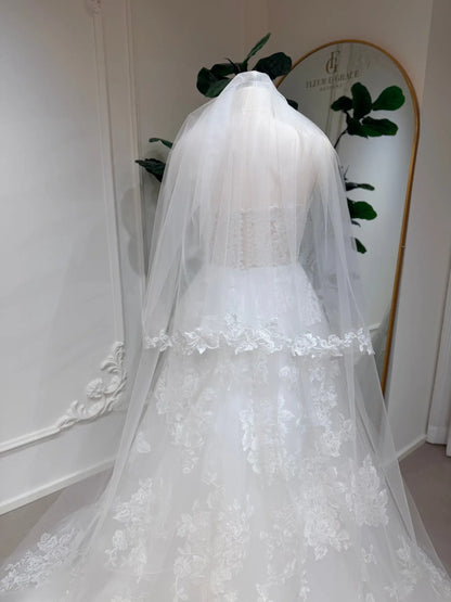 Strapless A-line wedding dress with floral lace appliqués, button-back bodice, and a matching sheer tulle veil.