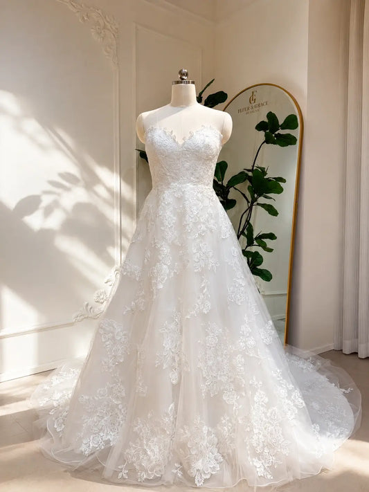 Strapless A-line wedding dress with a sweetheart neckline, floral lace appliqués, and a tulle chapel train on a mannequin.