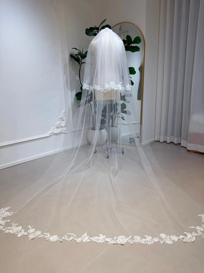 Cathedral-length white bridal veil in soft illusion tulle with delicate floral lace edging on a mannequin.