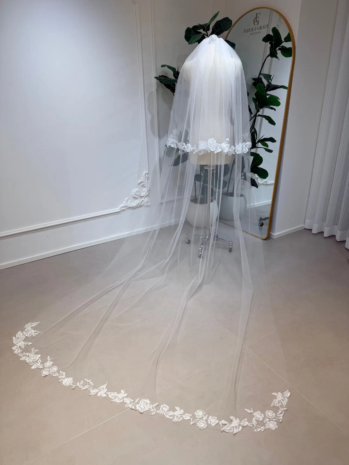 Cathedral-length white bridal veil in soft tulle with delicate floral lace edging on a mannequin.