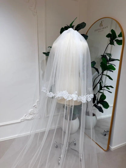 Cathedral-length white bridal veil in soft illusion tulle with delicate floral lace edging on a mannequin.