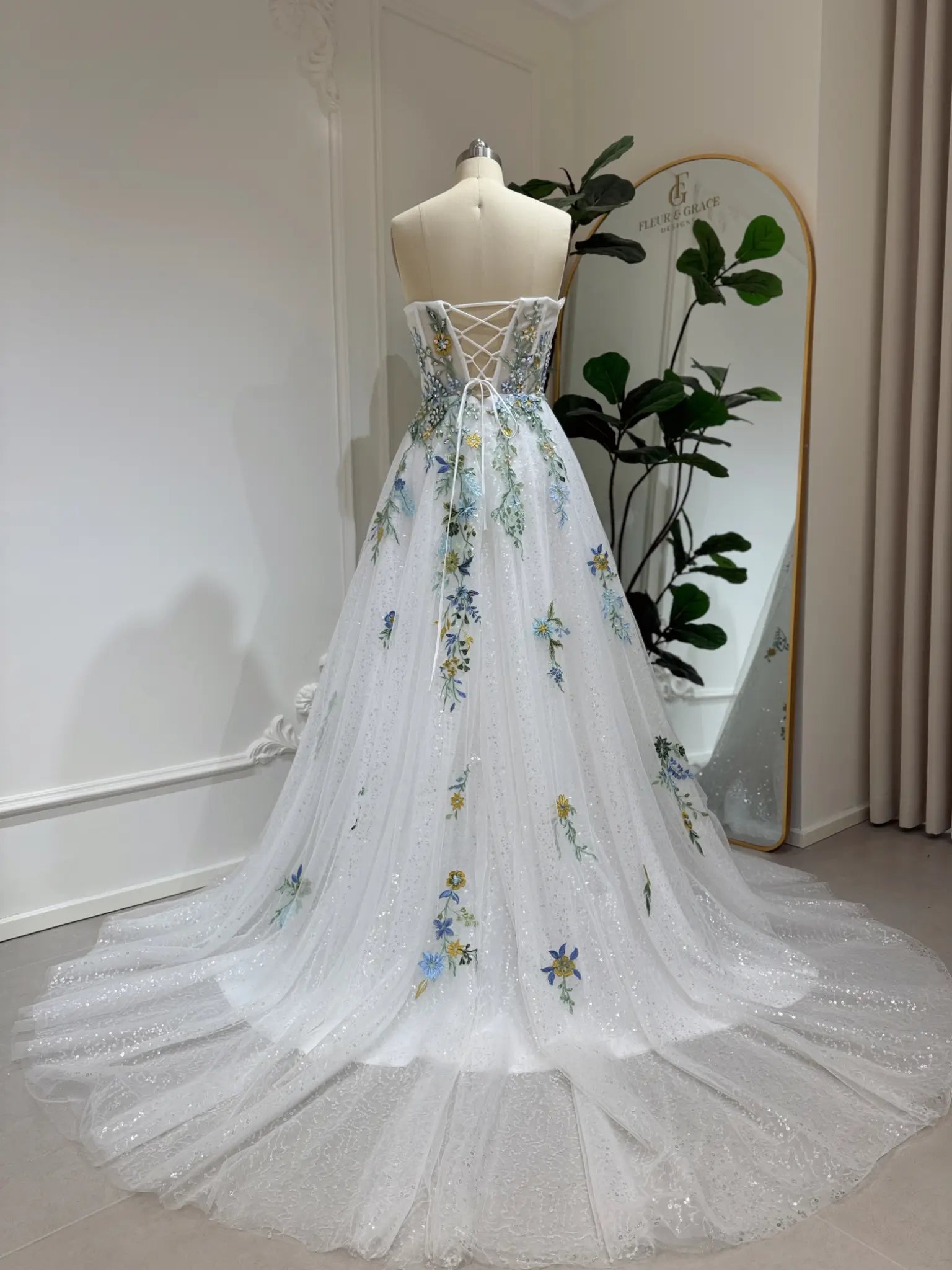 Whimsical white wedding gown with colorful floral embroidery, sparkly tulle, and a lace-up back on a dress form.