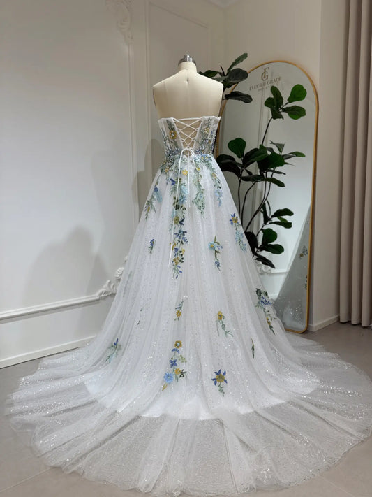 Whimsical white wedding gown with colorful floral embroidery, sparkly tulle, and a lace-up back on a dress form.