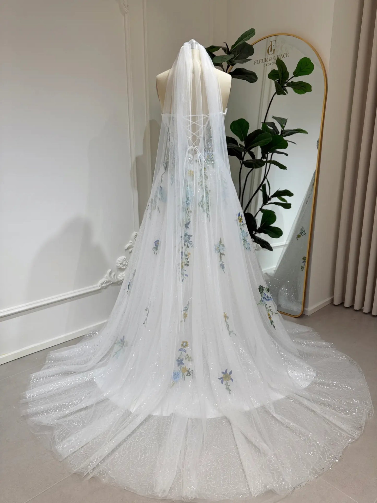 Whimsical white wedding gown with floral embroidery, sparkly tulle, and a lace-up back on a mannequin.