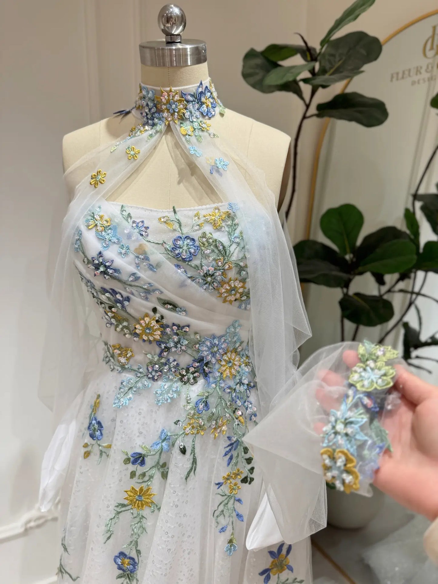 Whimsical white wedding dress with colorful floral embroidery, beaded details, illusion neckline, and flowing tulle.