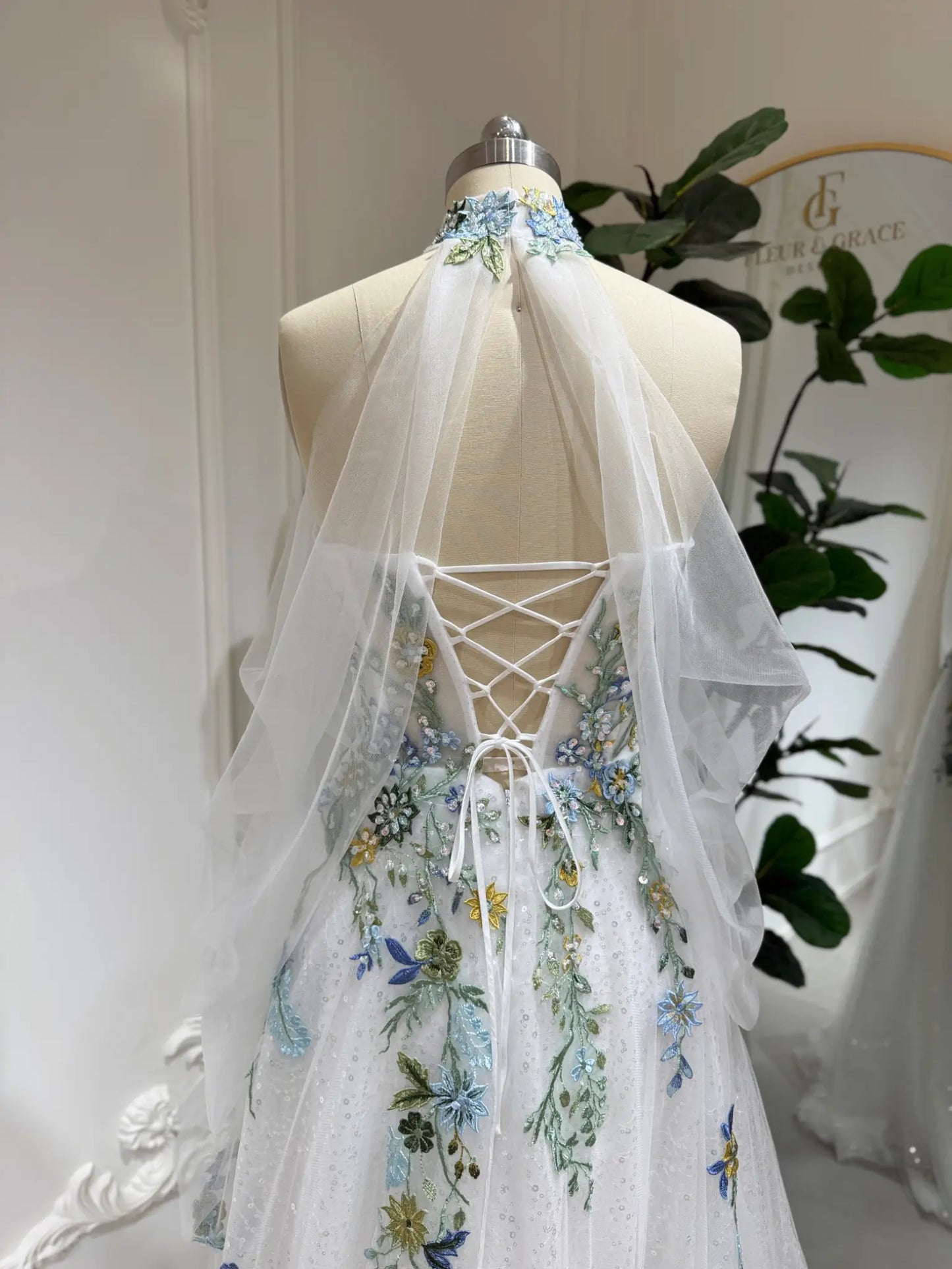 Whimsical wedding dress with colorful floral embroidery, illusion neckline, and adjustable lace-up back on a mannequin.