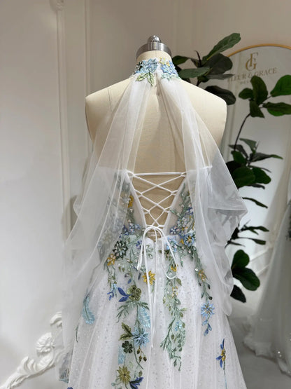 Whimsical wedding dress with colorful floral embroidery, illusion neckline, and adjustable lace-up back on a mannequin.