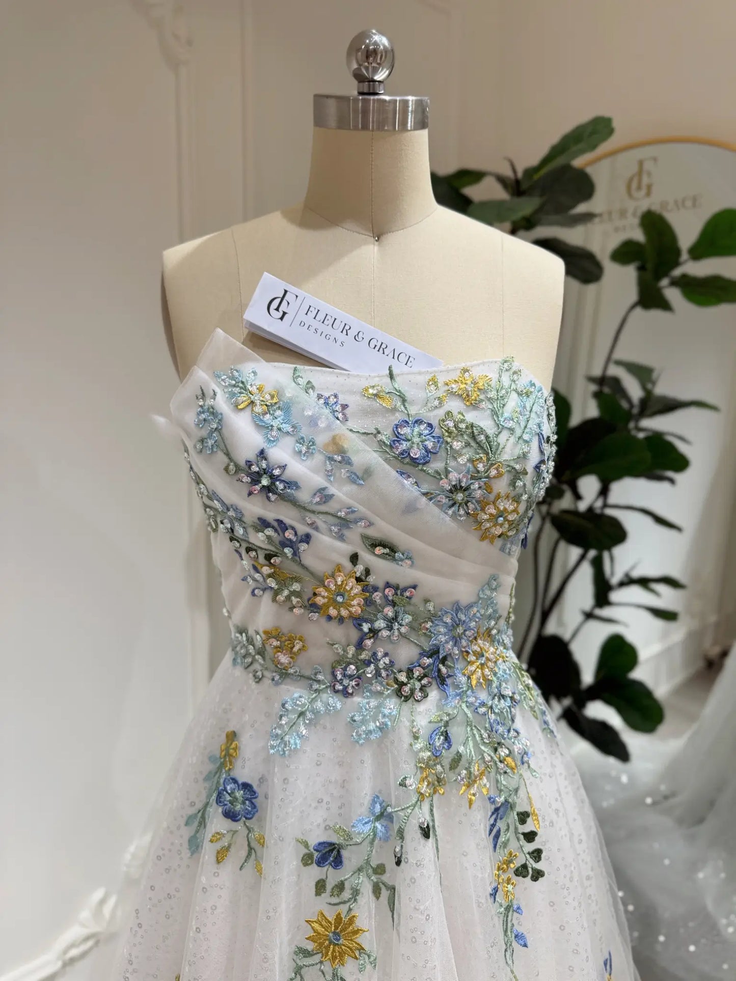 Whimsical white wedding gown featuring colorful floral embroidery, beaded accents, and sparkly tulle on a mannequin.