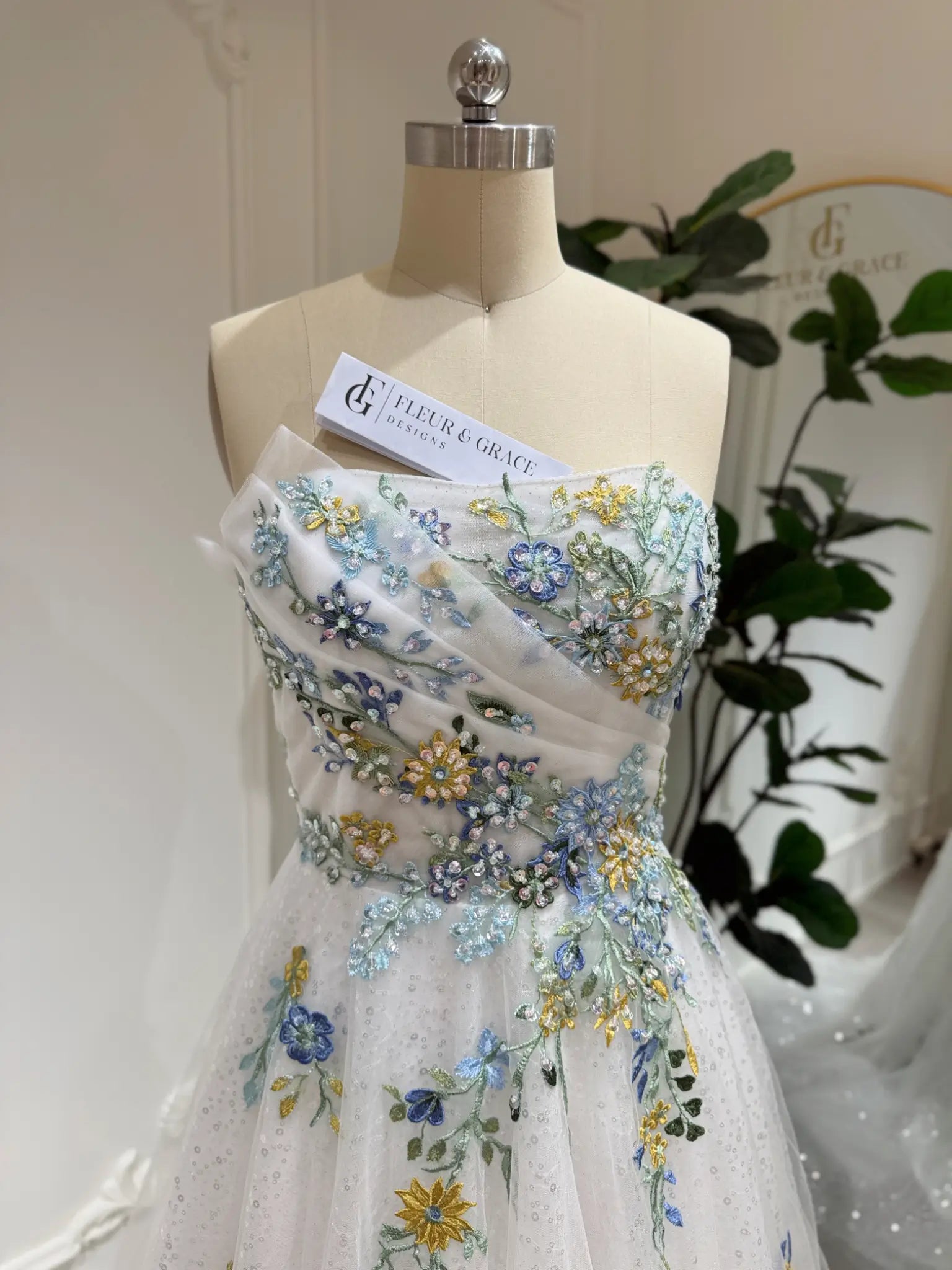 Whimsical white wedding gown featuring colorful floral embroidery, beaded accents, and sparkly tulle on a mannequin.