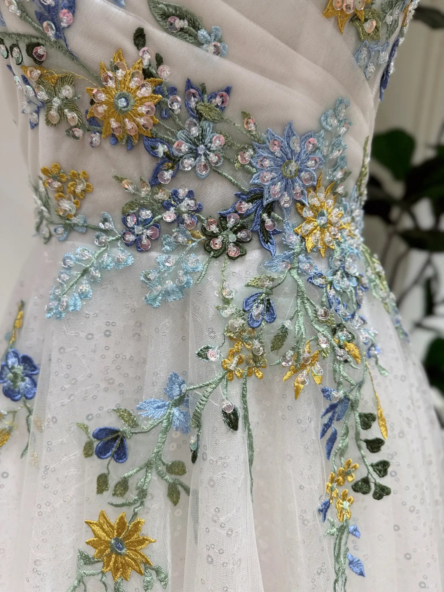 Whimsical wedding dress featuring intricate blue and yellow floral embroidery, sparkling tulle, and handmade beadwork.