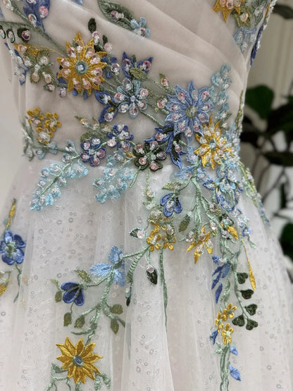 Whimsical wedding dress featuring intricate blue and yellow floral embroidery, sparkling tulle, and handmade beadwork.