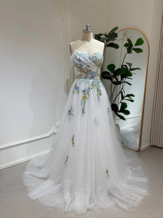 Whimsical white wedding gown with colorful floral embroidery, sparkly tulle, and a flowing skirt on a mannequin.