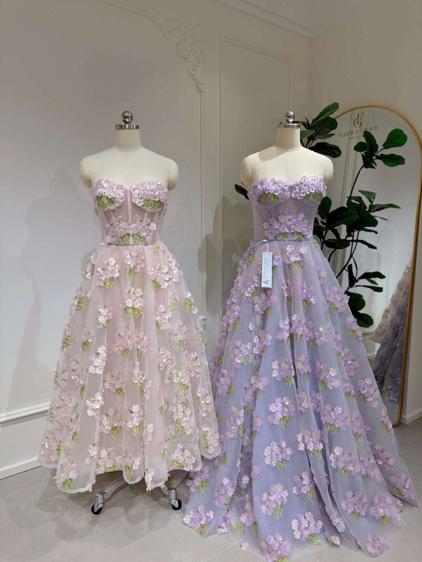 Two strapless sweetheart gowns featuring 3D hydrangea floral lace, sparkly mesh, and structured bodices on mannequins.