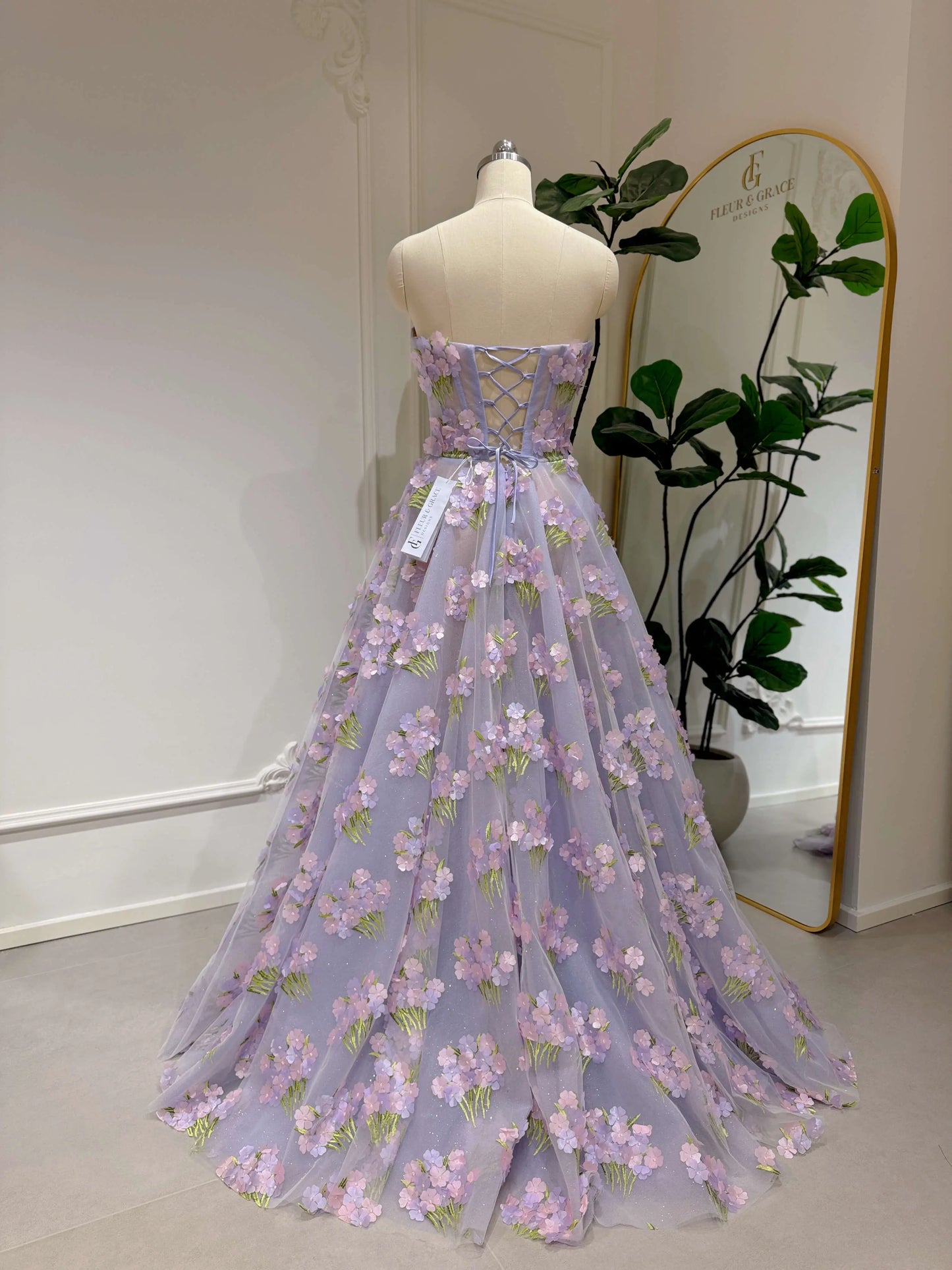 Lavender floor-length gown with 3D hydrangea floral lace, sparkly mesh lining, and a strapless lace-up back on a mannequin.