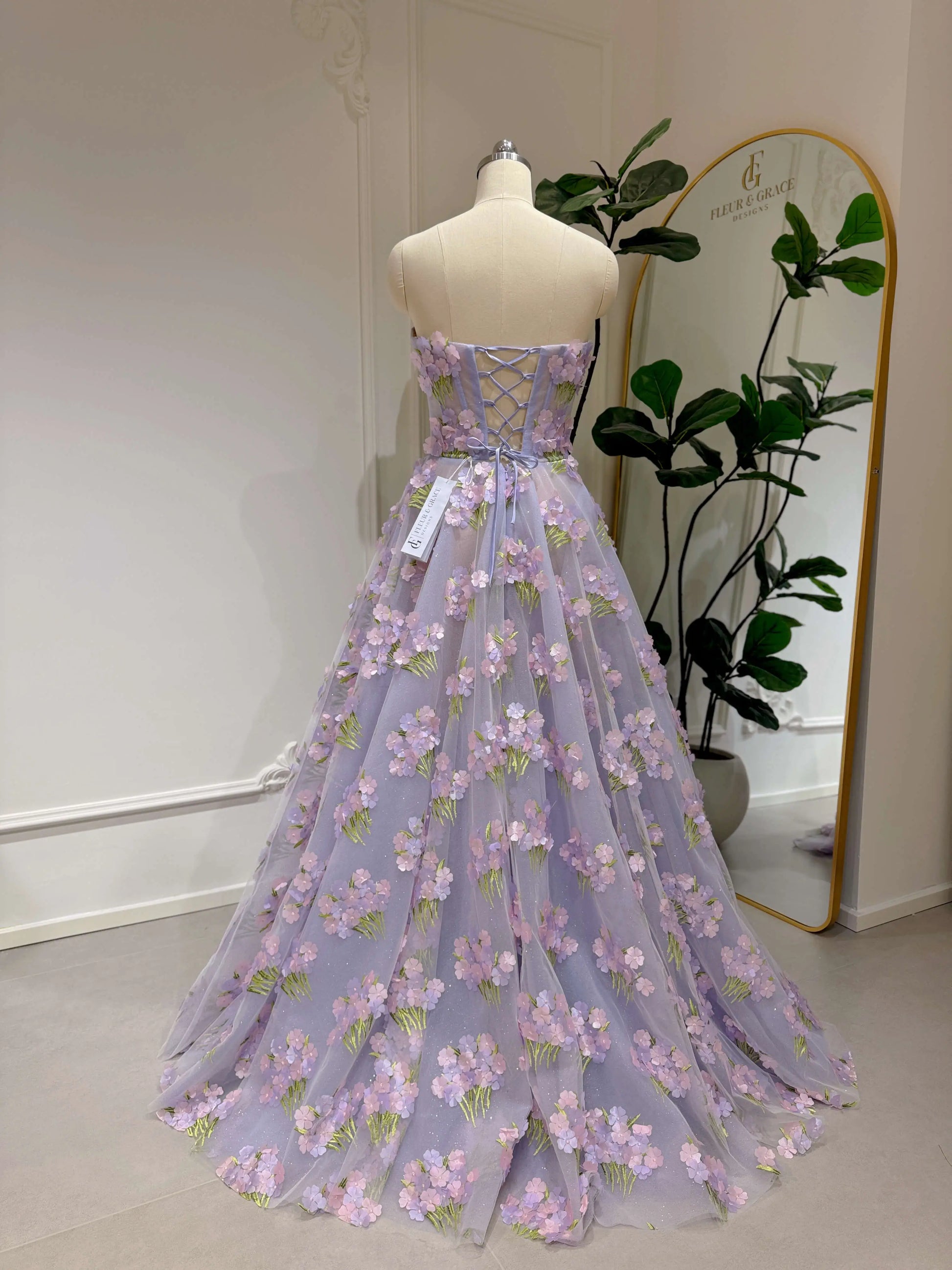 Lavender floor-length gown with 3D hydrangea floral lace, sparkly mesh lining, and a strapless lace-up back on a mannequin.