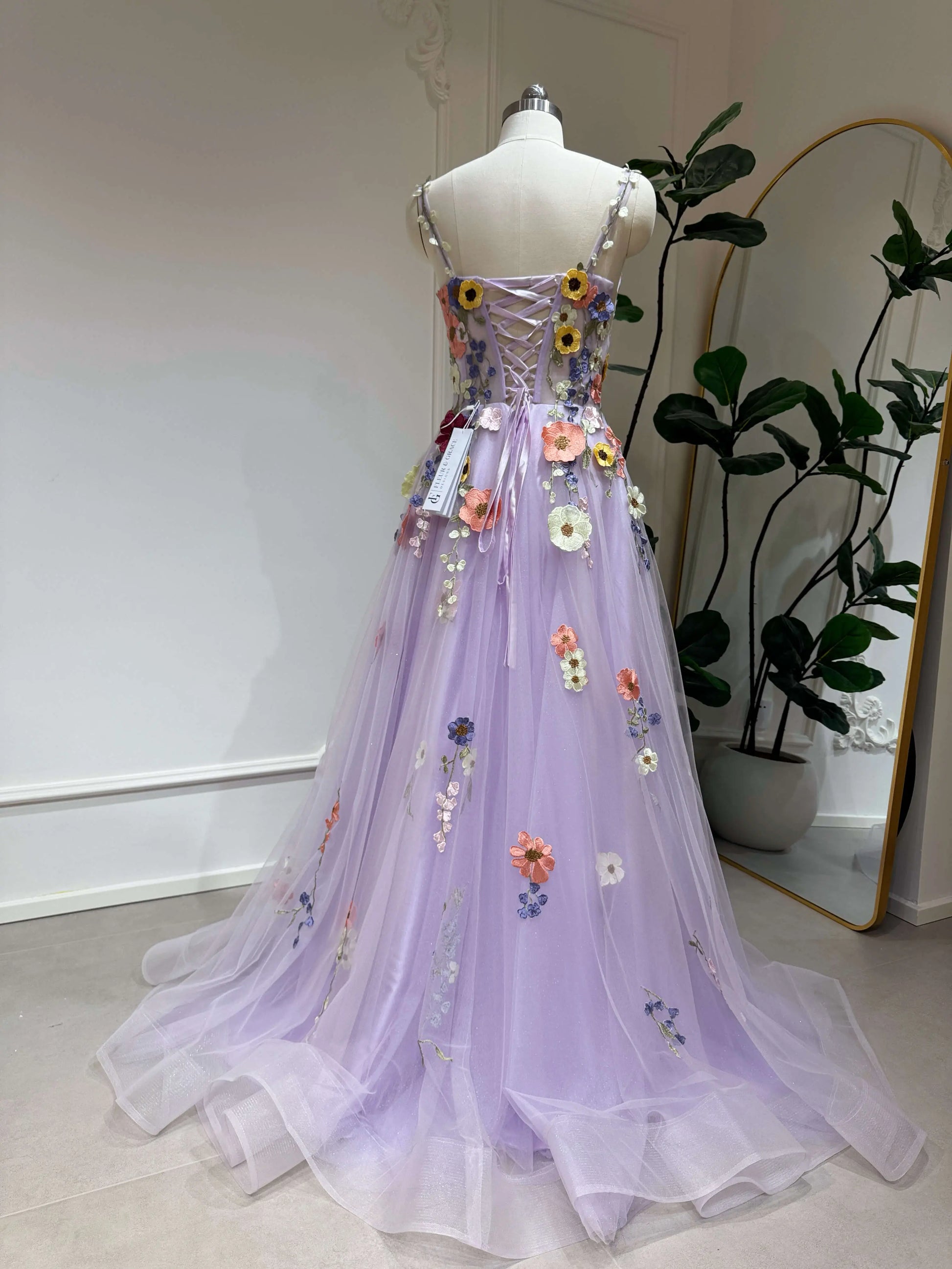 Lavender tulle formal gown with floral embroidery, lace-up back, and sparkly skirt on a mannequin.
