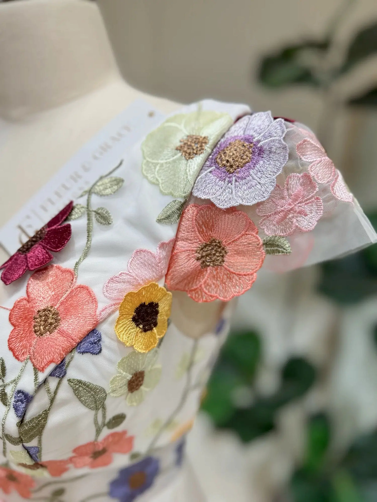 White wedding dress bodice with colorful floral embroidery in pink, yellow, and lavender on cap sleeves.
