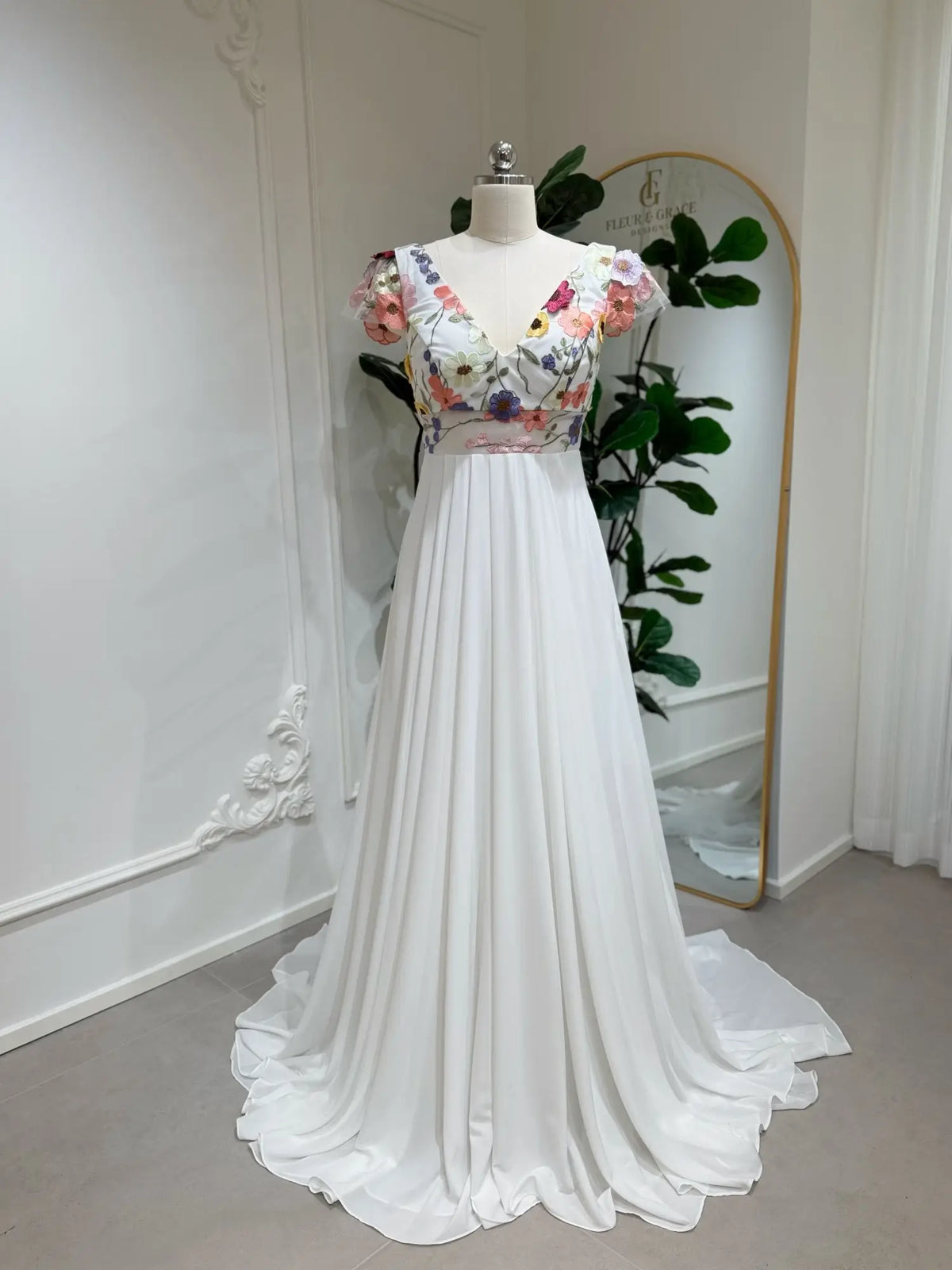 White chiffon A-line wedding dress with a V-neck bodice featuring colorful floral embroidery and cap sleeves.