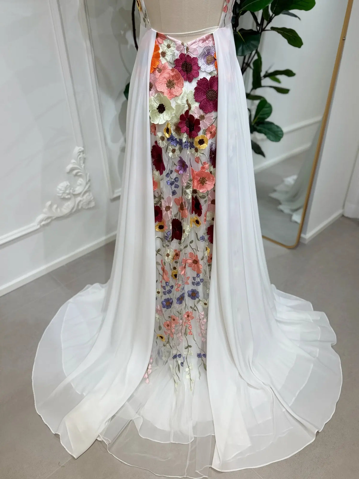White chiffon wedding dress with a vibrant, multi-colored floral embroidered back panel and flowing train.