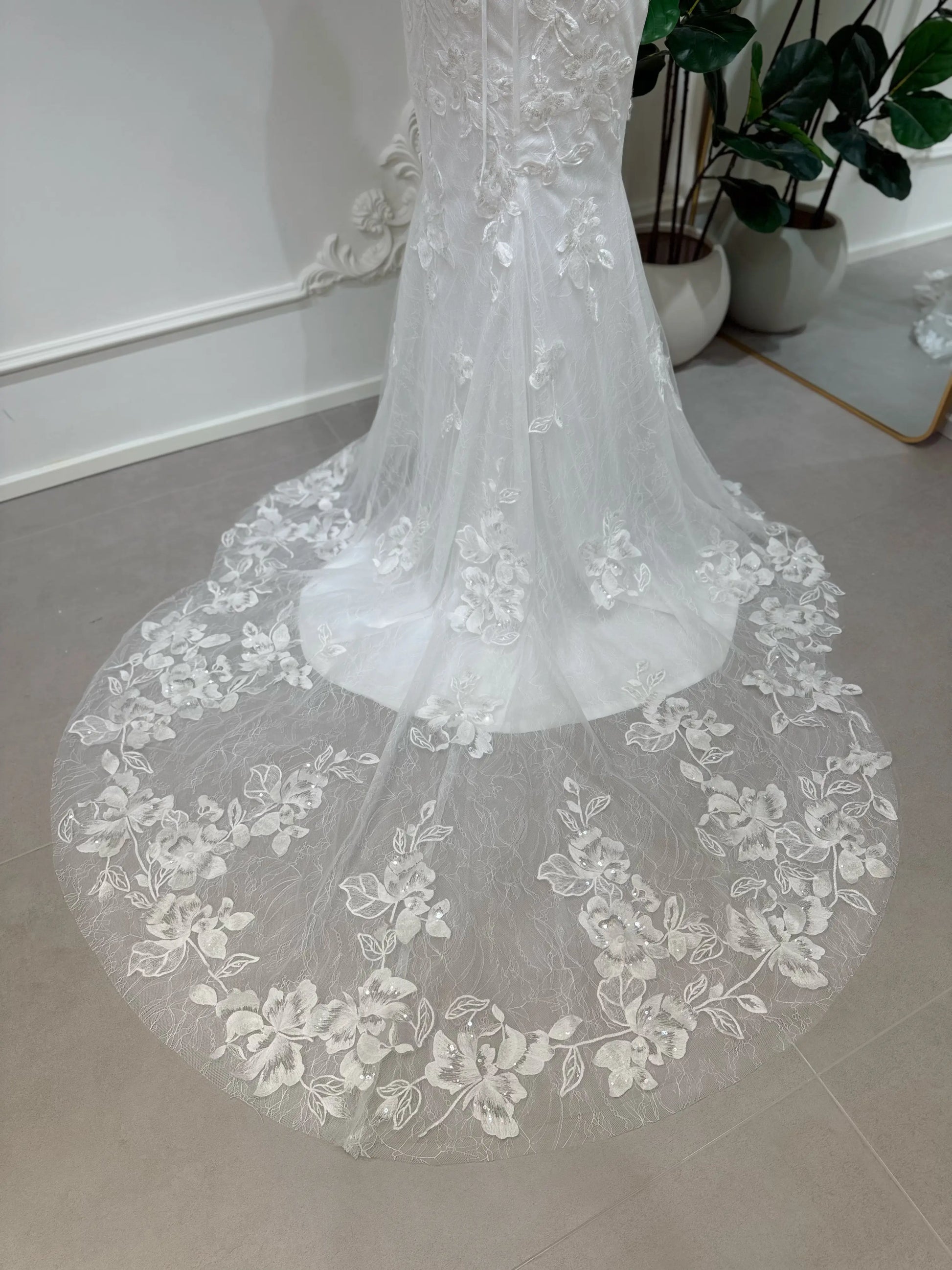 Bridal mannequin wearing the Lena Gown FG030 by Fleur&Grace Designs—a mermaid lace wedding dress with off-the-shoulder sleeves, sheer boned bodice, corset back, basque waistline, asymmetric hemline, and chapel-length train.