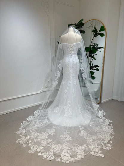 Off-the-shoulder mermaid wedding dress with lace, corset back, and long floral veil on a mannequin.