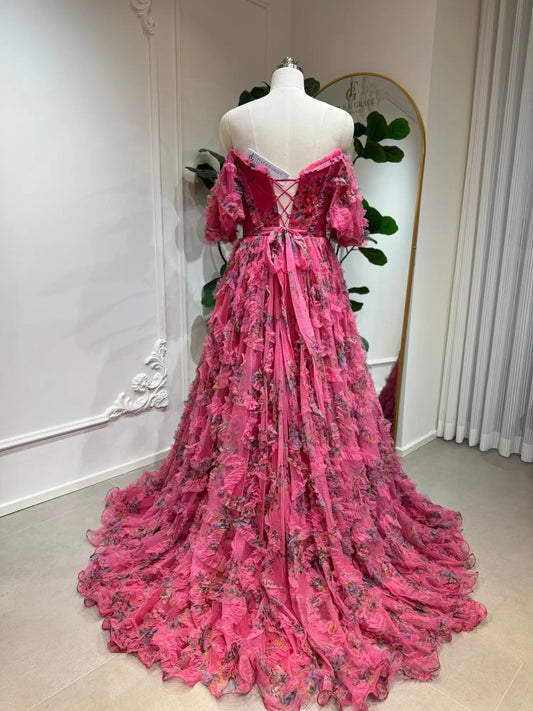Pink floral tulle gown with off-the-shoulder puff sleeves, ruffled skirt, and lace-up corset back on a mannequin.
