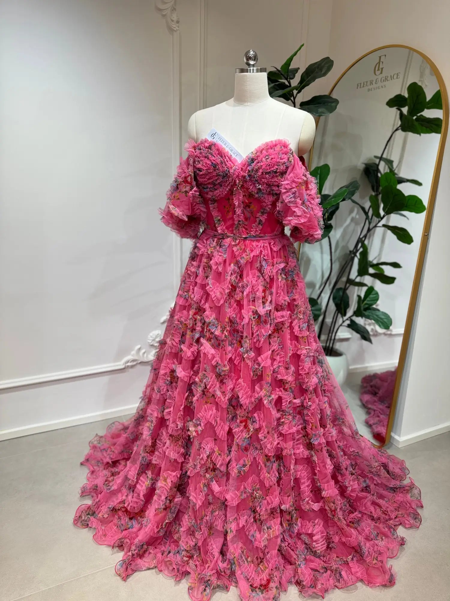 Pink floral tulle gown with off-the-shoulder puff sleeves, sweetheart corset bodice, and cascading ruffled A-line skirt.