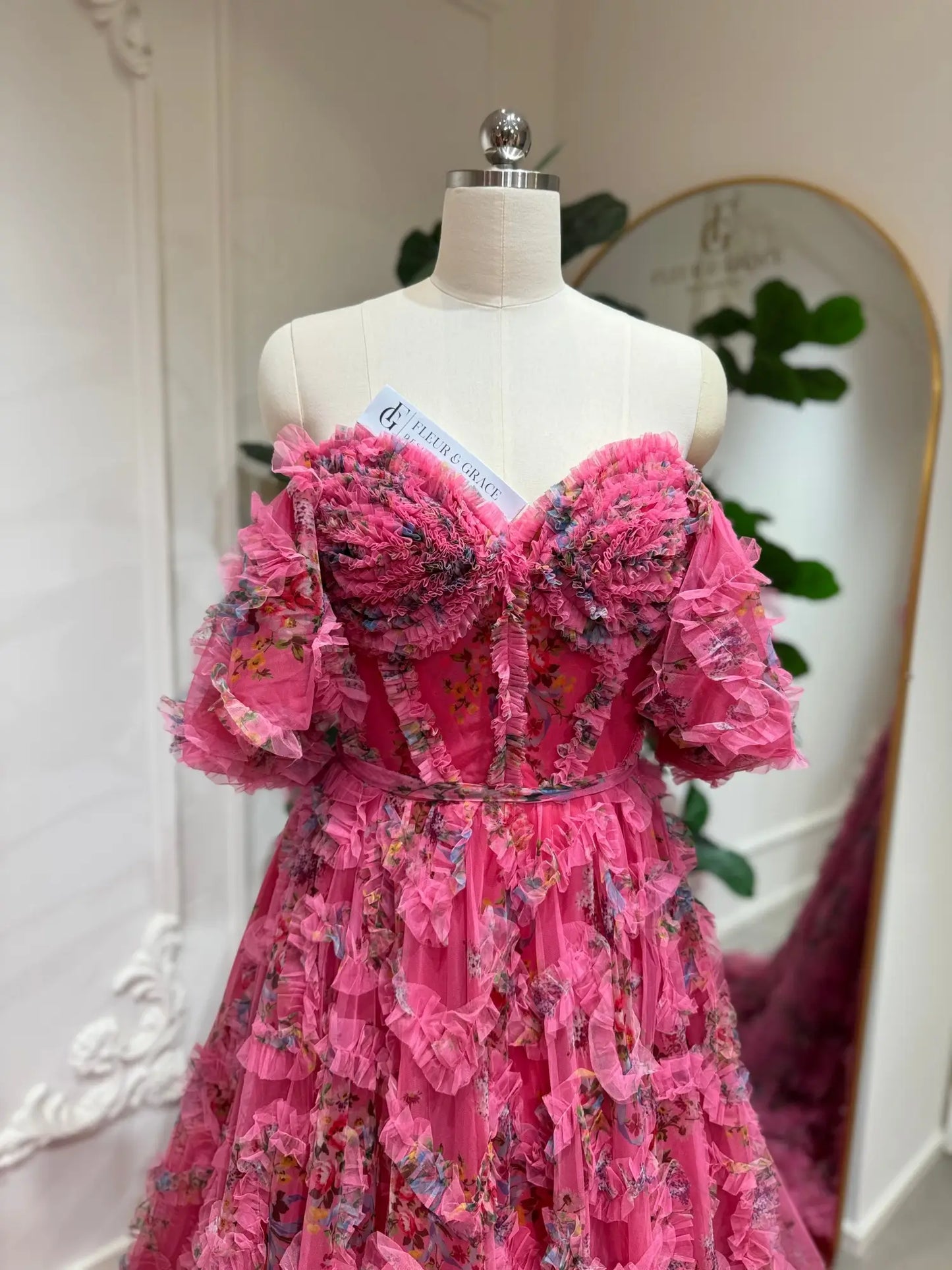 Pink floral tulle gown with an off-the-shoulder corset bodice, puff sleeves, and romantic ruffled detailing.
