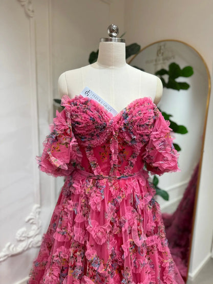Pink floral tulle gown with an off-the-shoulder corset bodice, puff sleeves, and romantic ruffled detailing.