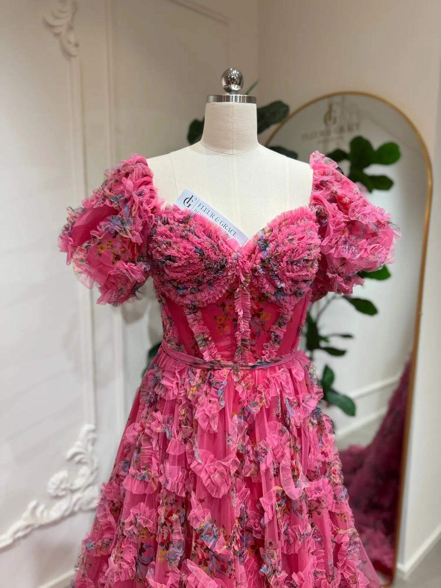 Pink floral tulle gown with off-the-shoulder puff sleeves, sweetheart corset bodice, and cascading ruffle details.