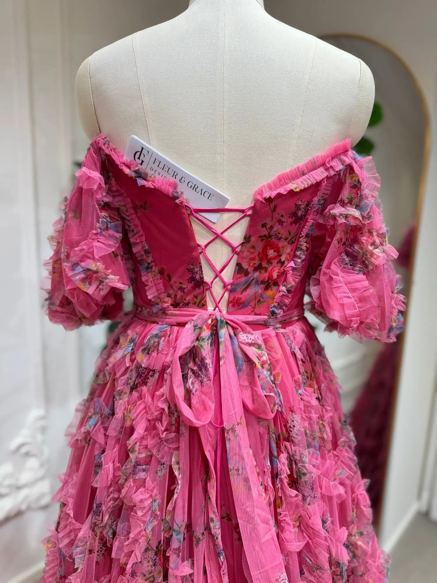 Pink floral tulle gown featuring off-the-shoulder puff sleeves, cascading ruffles, and an adjustable lace-up corset back.
