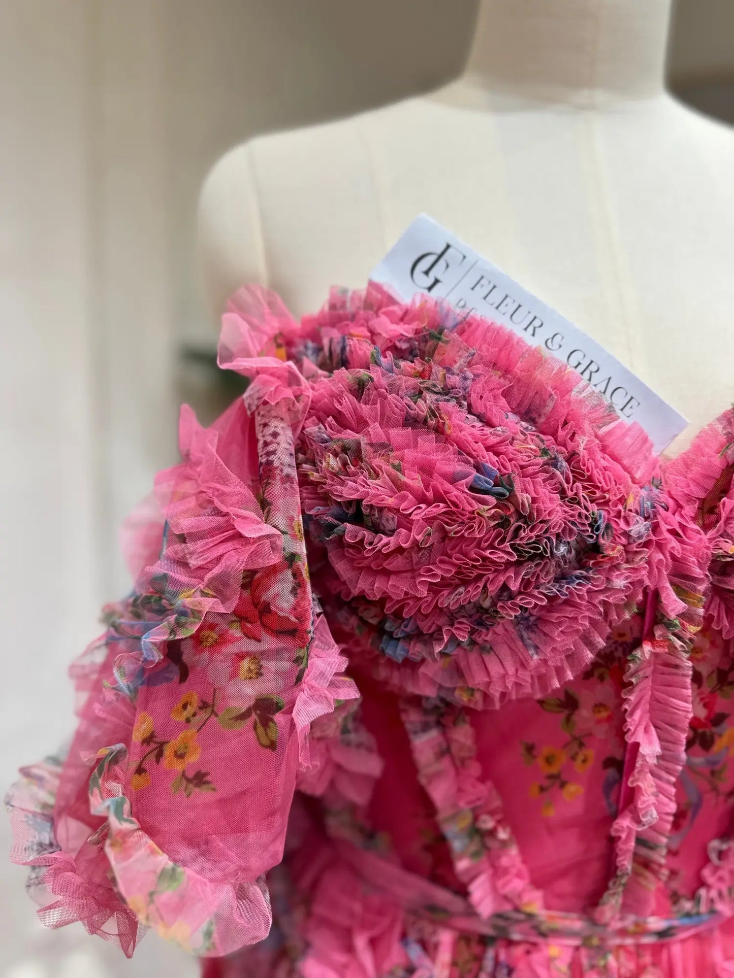 Pink floral tulle gown featuring a sweetheart corset bodice, ruffled off-the-shoulder puff sleeves, and romantic detailing.