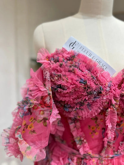 Pink floral tulle gown featuring a sweetheart corset bodice, ruffled off-the-shoulder puff sleeves, and romantic detailing.