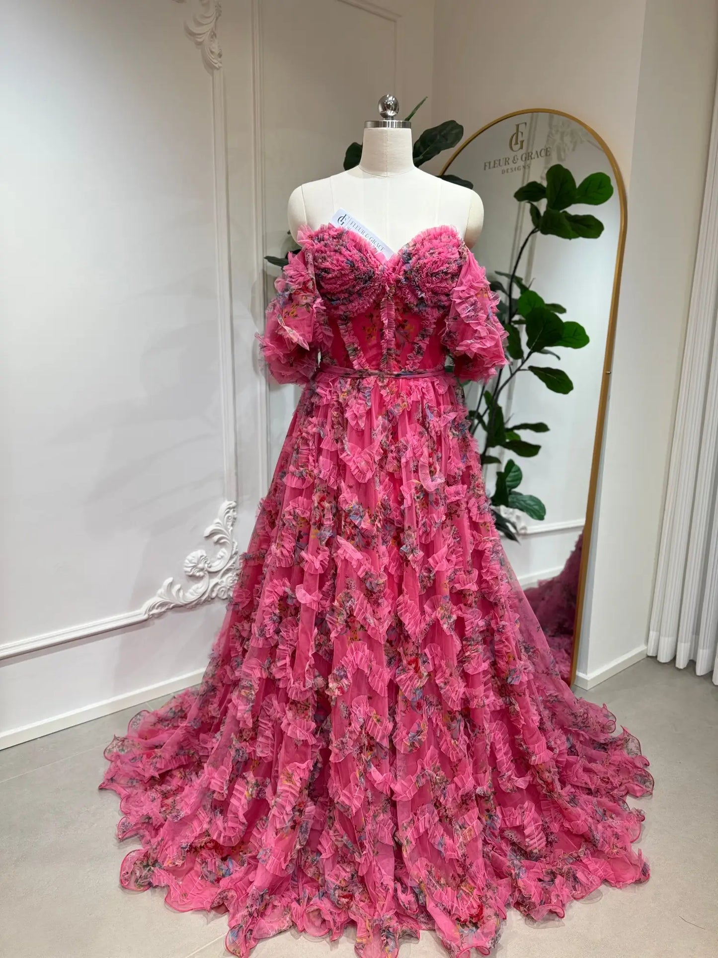 Pink floral tulle gown with off-the-shoulder puff sleeves, sweetheart corset bodice, and cascading ruffled A-line skirt.