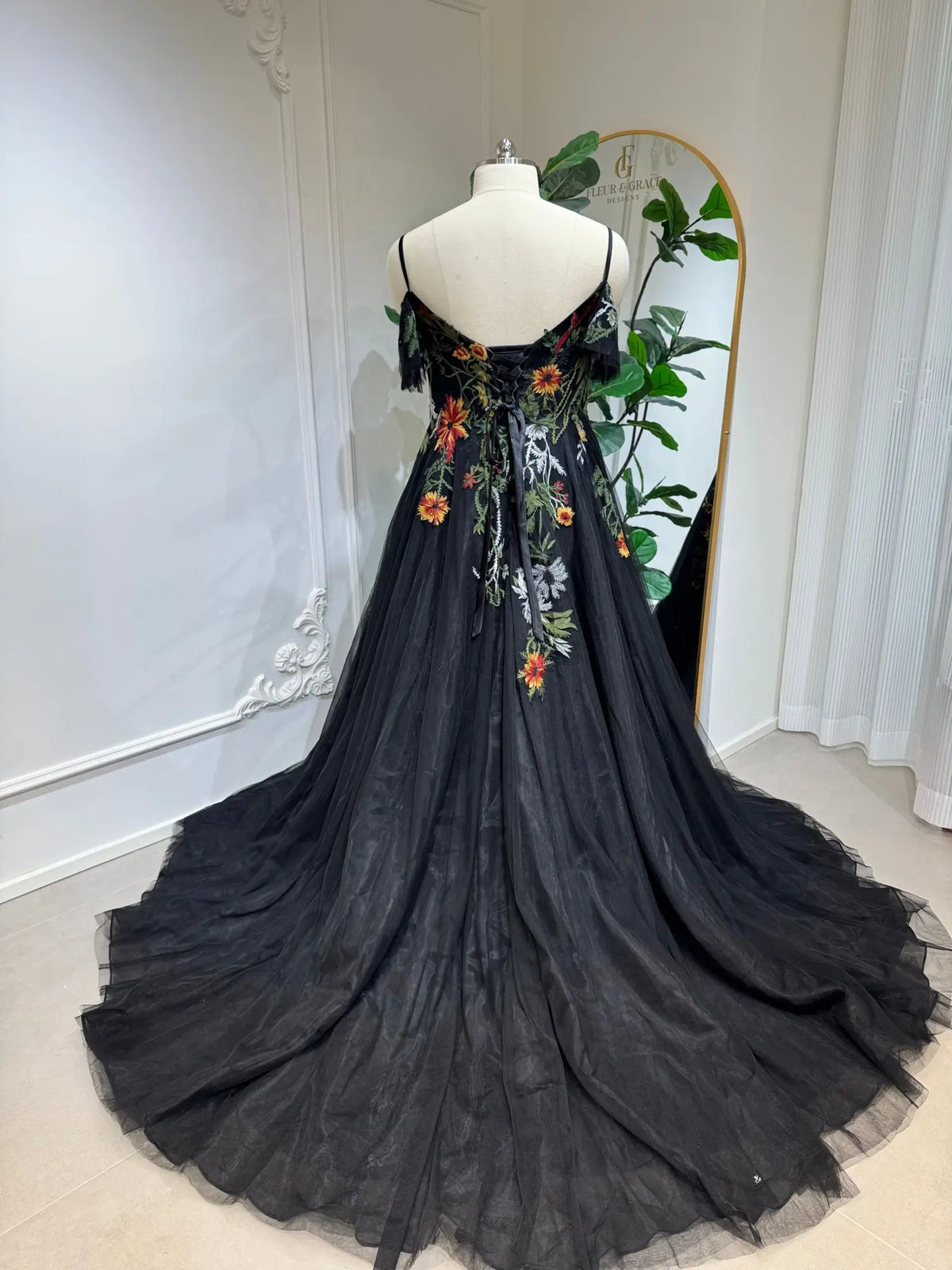 Black tulle wedding dress with vibrant floral embroidery, corset lace-up back, spaghetti straps, and flowing A-line skirt.