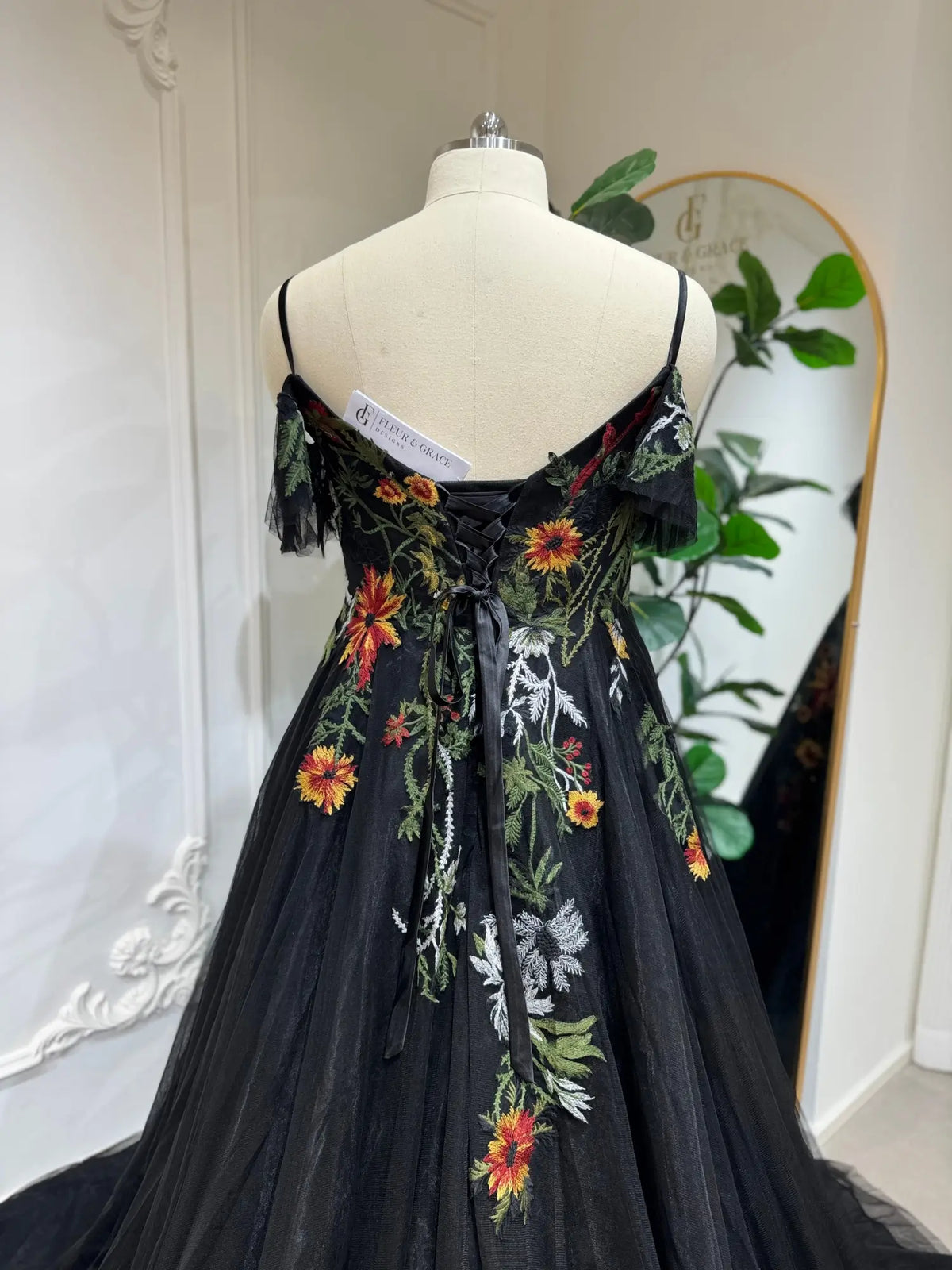 Black tulle wedding dress with vibrant floral embroidery, spaghetti straps, off-the-shoulder sleeves, and lace-up corset back.