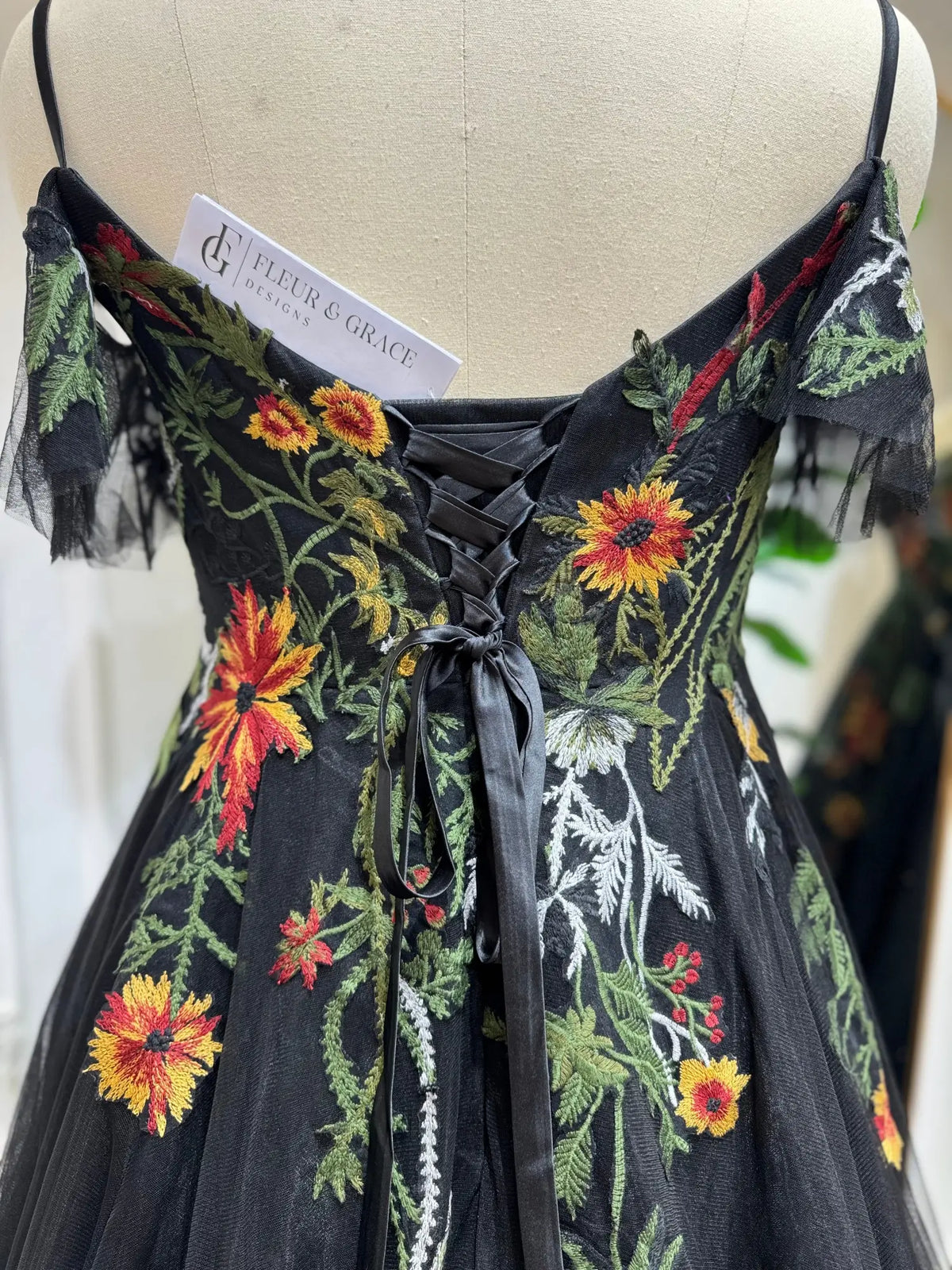 Black tulle wedding dress with vibrant floral embroidery, spaghetti straps, off-the-shoulder sleeves, and lace-up corset back.