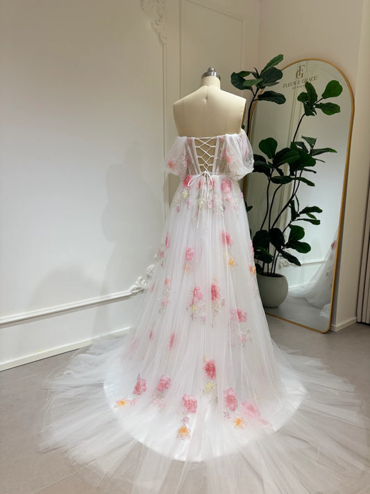 Pink tulle wedding gown with 3D floral appliqués, off-shoulder sleeves, lace-up back, and chapel-length train.