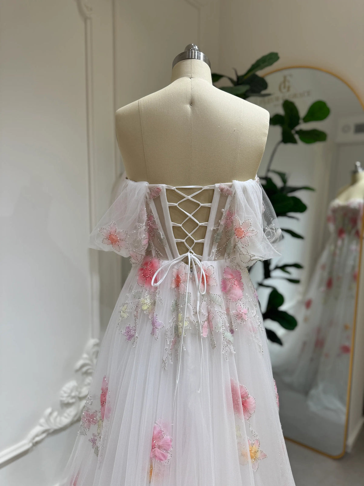 Luna Gown in white tulle with pink 3D floral appliqués, off-shoulder flutter sleeves, and a lace-up corset back.