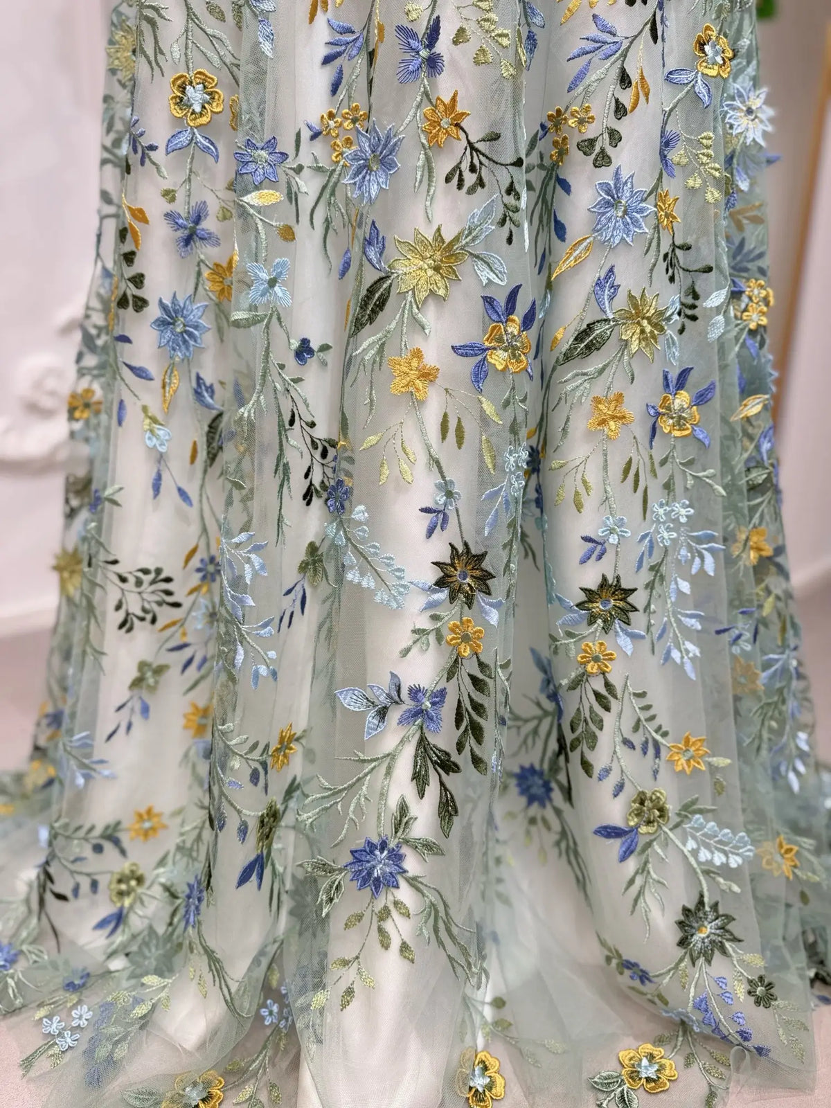 Meadow green tulle wedding dress featuring intricate blue, yellow, and green floral embroidery in an A-line silhouette.