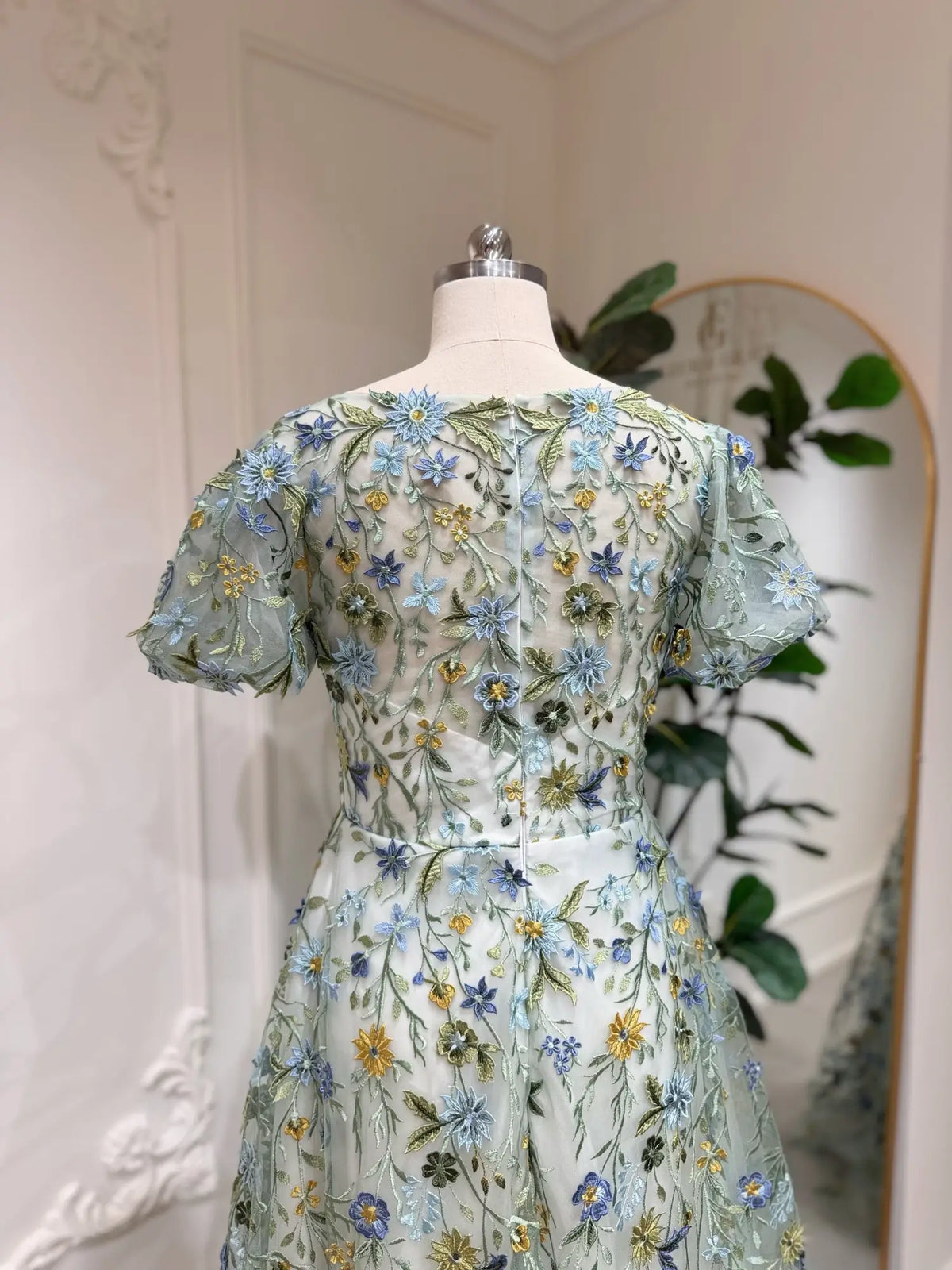 Meadow green tulle wedding dress featuring intricate blue and yellow floral embroidery and romantic puff sleeves.