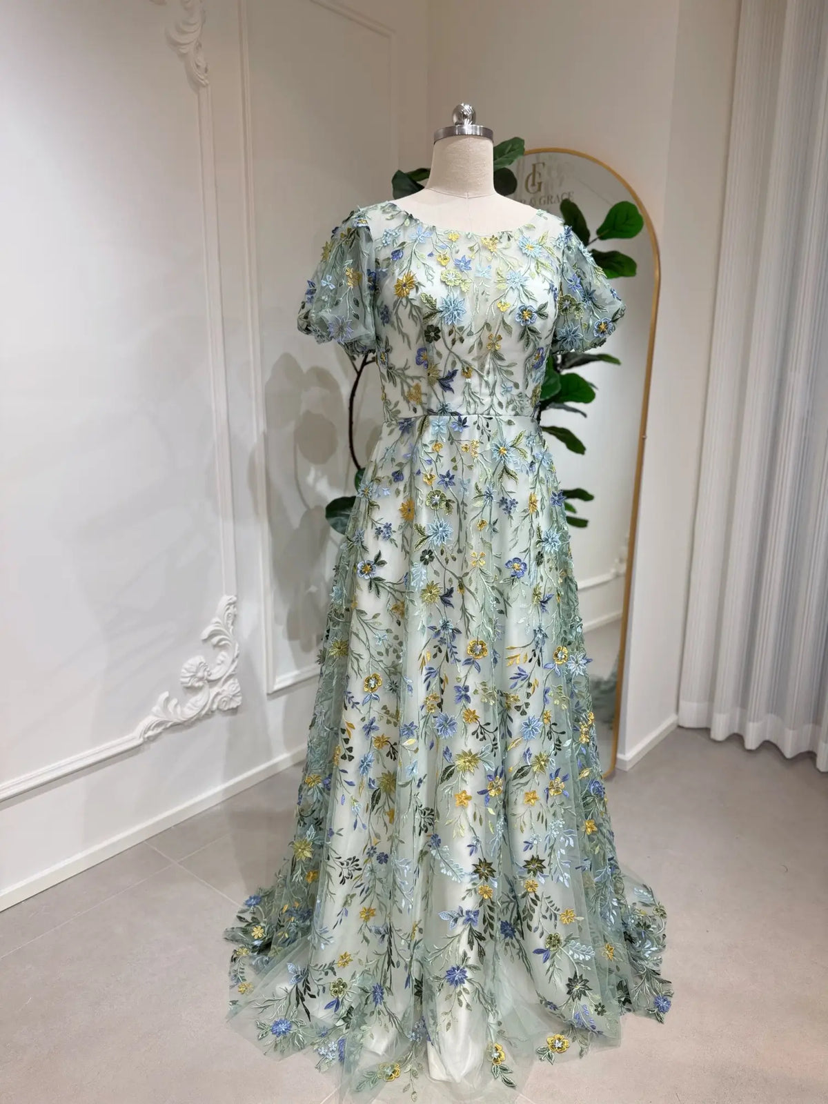 Meadow green tulle wedding gown featuring intricate blue and yellow floral embroidery, puff sleeves, and A-line silhouette.