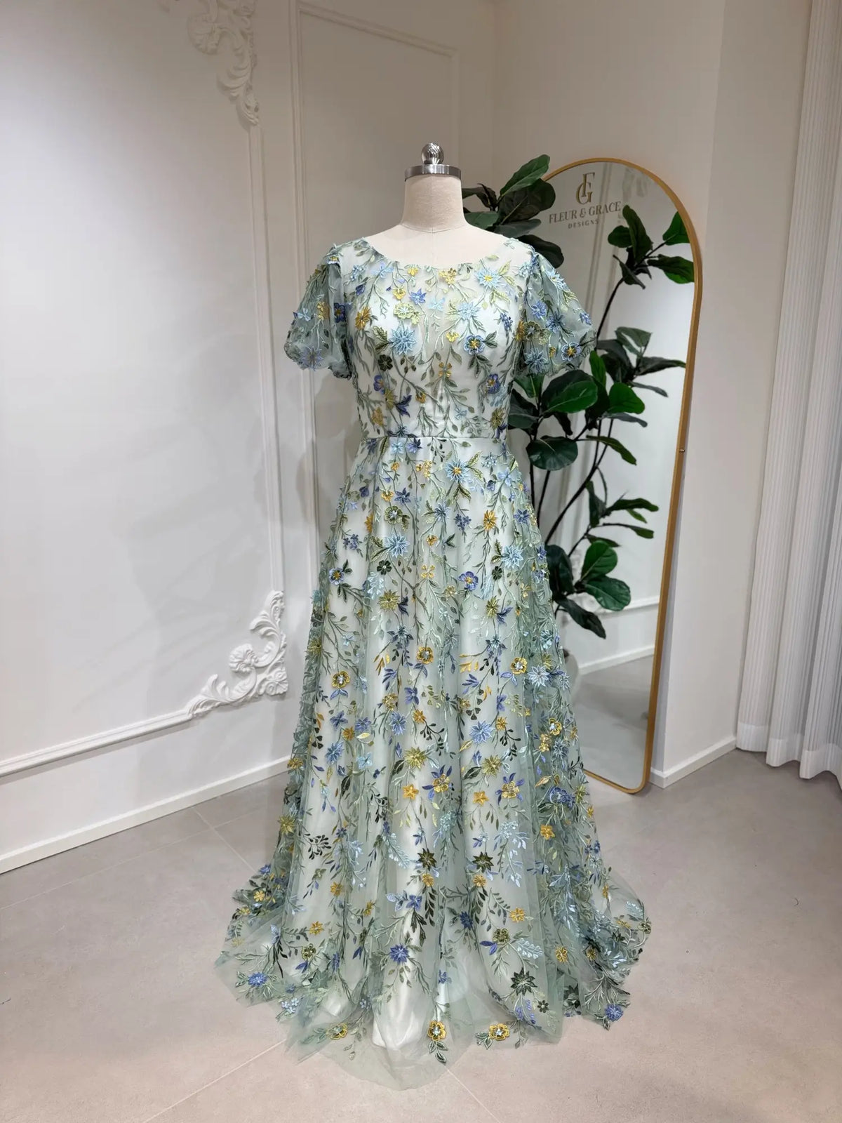 Meadow green tulle wedding gown featuring intricate blue and yellow floral embroidery, puff sleeves, and an A-line silhouette.