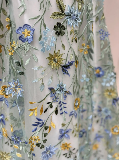Meadow wedding dress featuring intricate blue, yellow, and green floral embroidery on airy, layered tulle fabric.